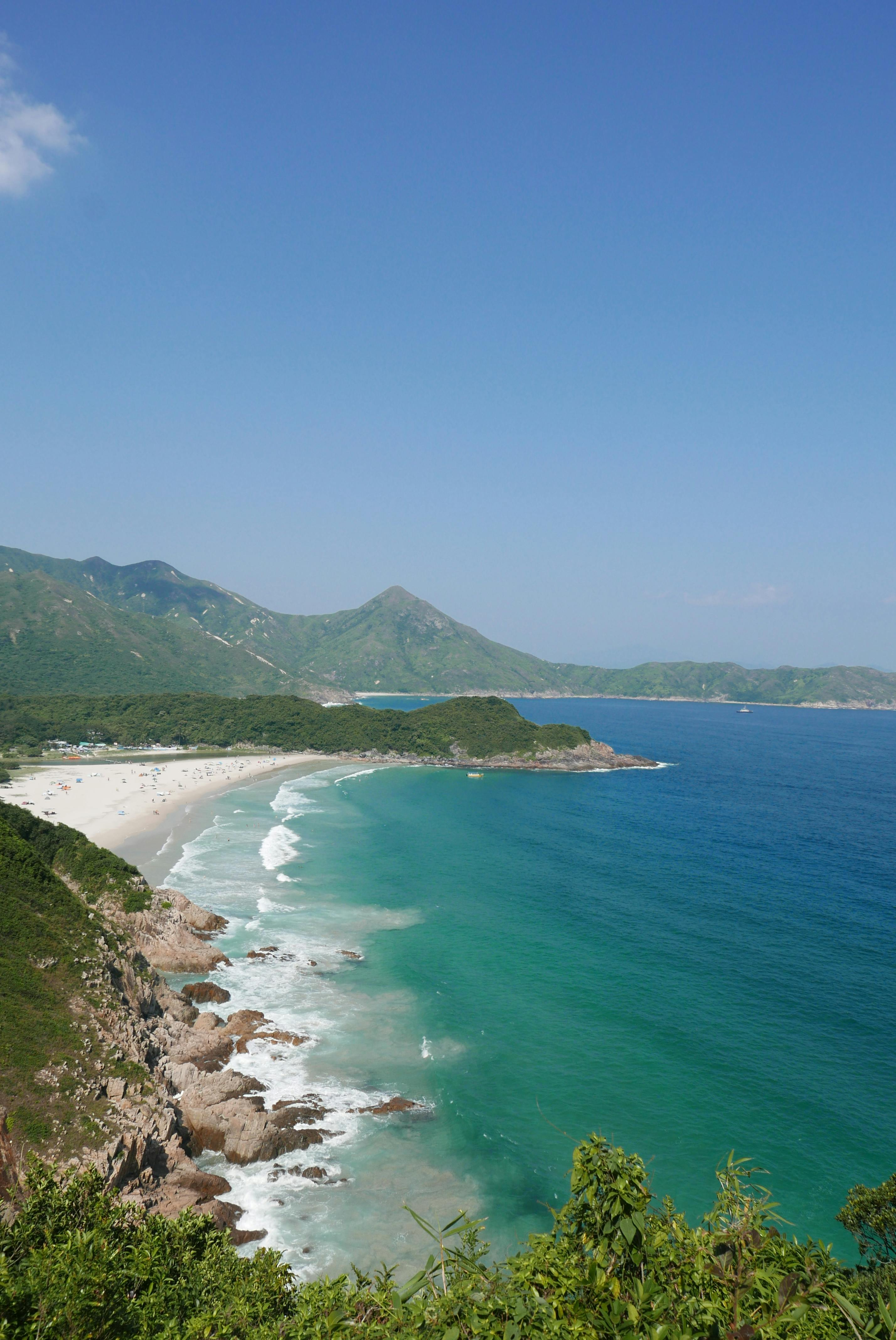 Breathtaking view of Sai Wan Beach with clear blue waters and lush green mountains in New Territories, Hong Kong.