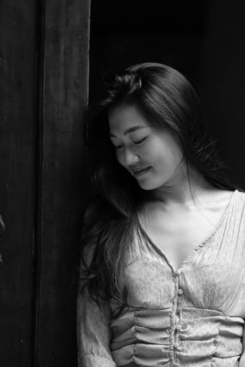 Free Black and white portrait of an Asian woman leaning against a wall with a serene expression. Stock Photo