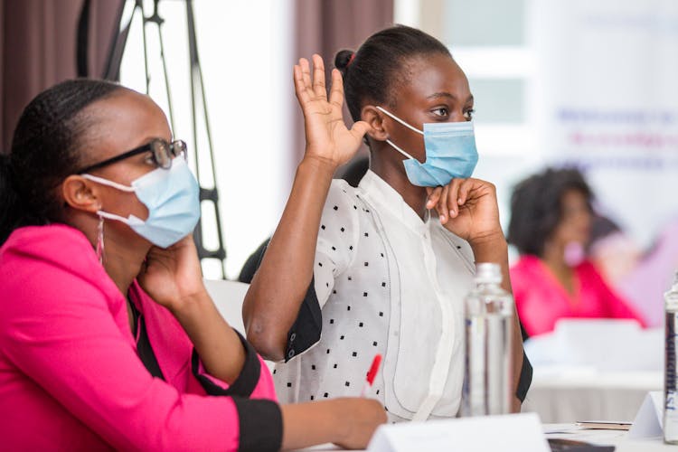 Women Sitting In Masks And Raising Hand