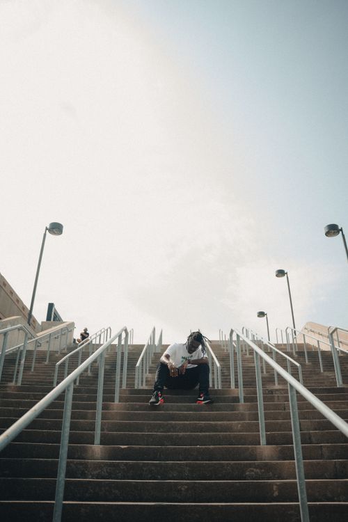 Free A man in white t-shirt and black pants sits on concrete steps surrounded by metal railings. Stock Photo