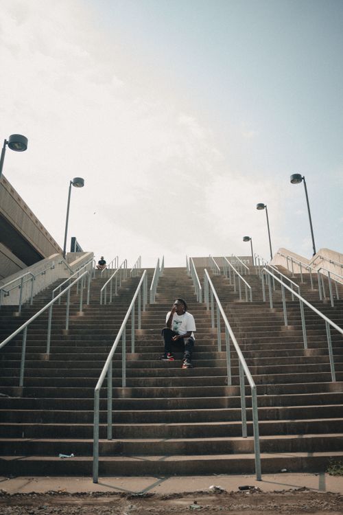 Free A man sits on a city staircase surrounded by urban architecture and railings. Stock Photo