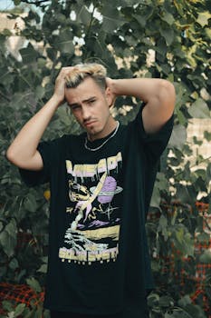 Stylish young man posing confidently outdoors, wearing a graphic t-shirt surrounded by lush greenery.