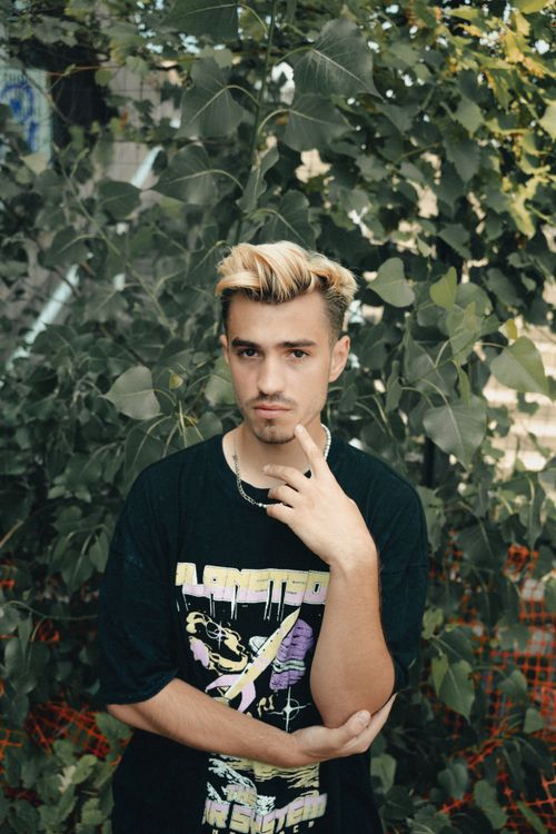 Free Blonde young man with facial hair posing outdoors against lush foliage. Stock Photo