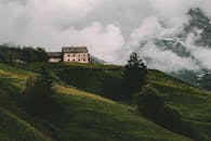 迷人的乡村房屋坐落在绿草如茵的小山上，背景是云雾缭绕的群山