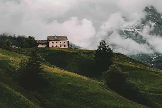 迷人的乡村房屋坐落在绿草如茵的小山上，背景是云雾缭绕的群山