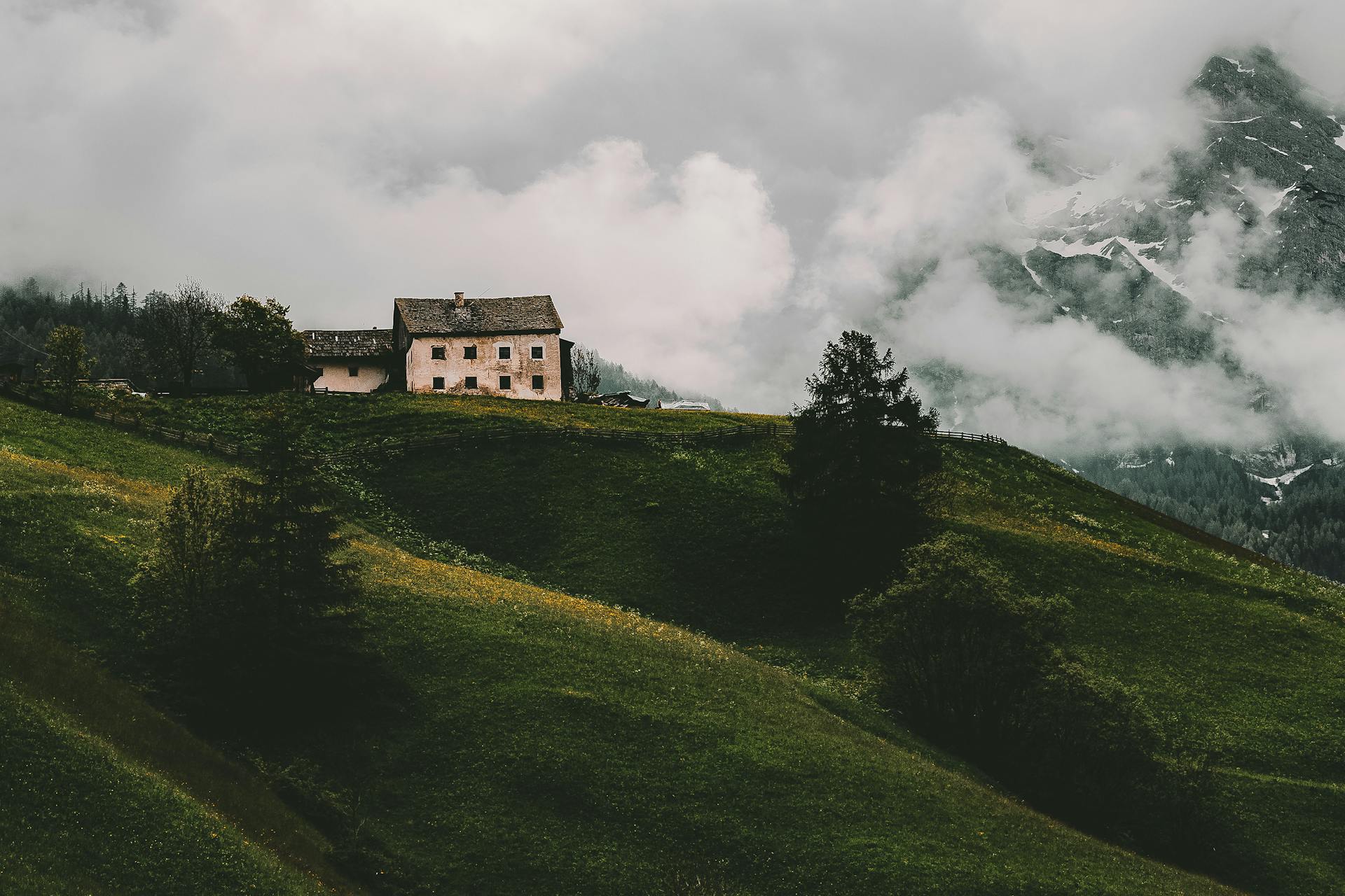 Charming rural house on a grassy hill with misty mountains and clouds in the background.