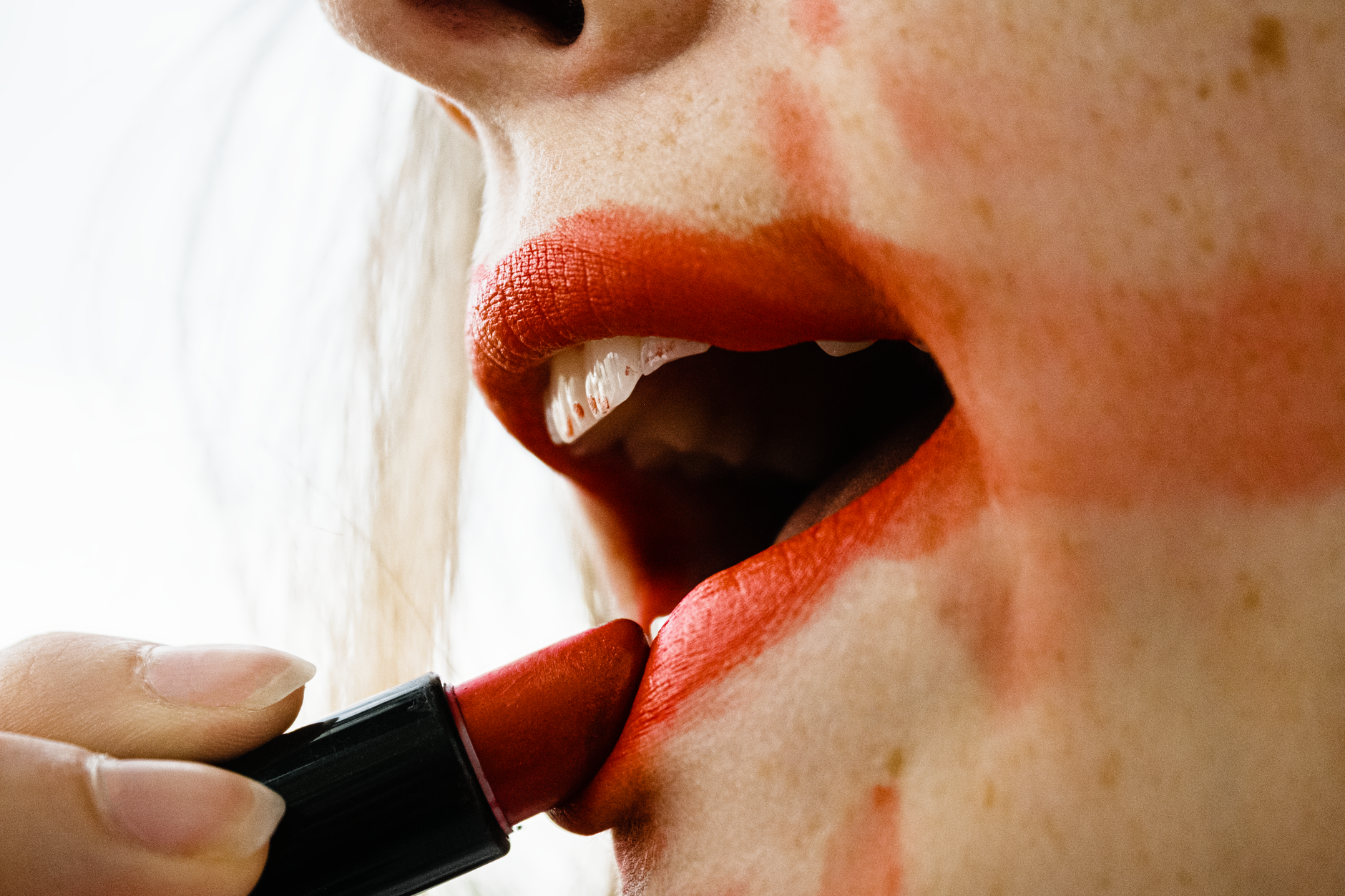 Close-up shot of a woman applying bold red lipstick with messy smudges around lips.