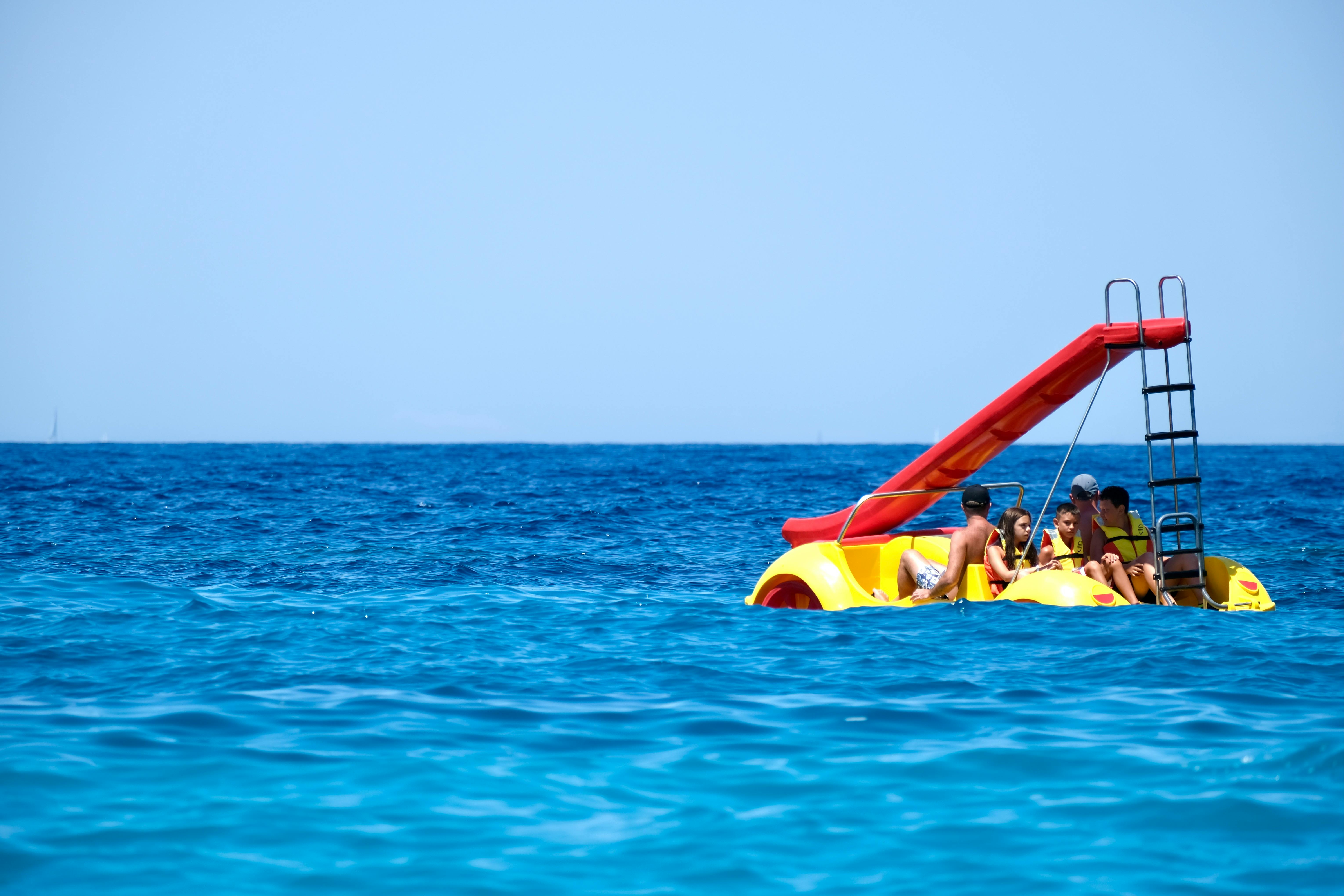 2 person riding yellow and red inflatable boat on sea