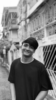 A black and white portrait of a smiling young man in a casual urban street setting.