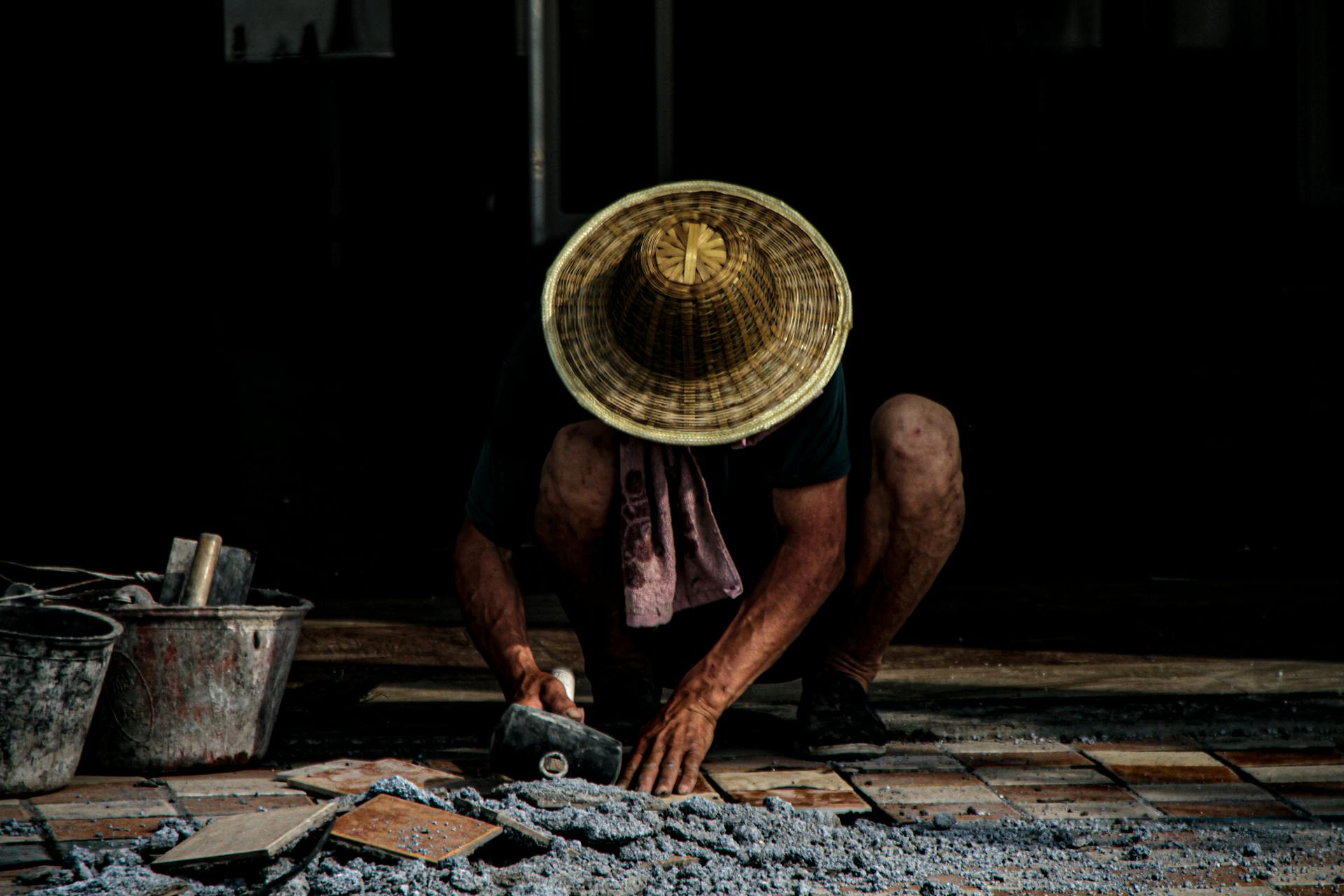 A mason installing tiles outdoors, wearing a traditional hat. Focus on craftsmanship.