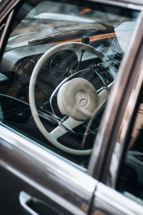 Free Close-up of a vintage Mercedes Benz steering wheel seen through the car window, showcasing classic design. Stock Photo