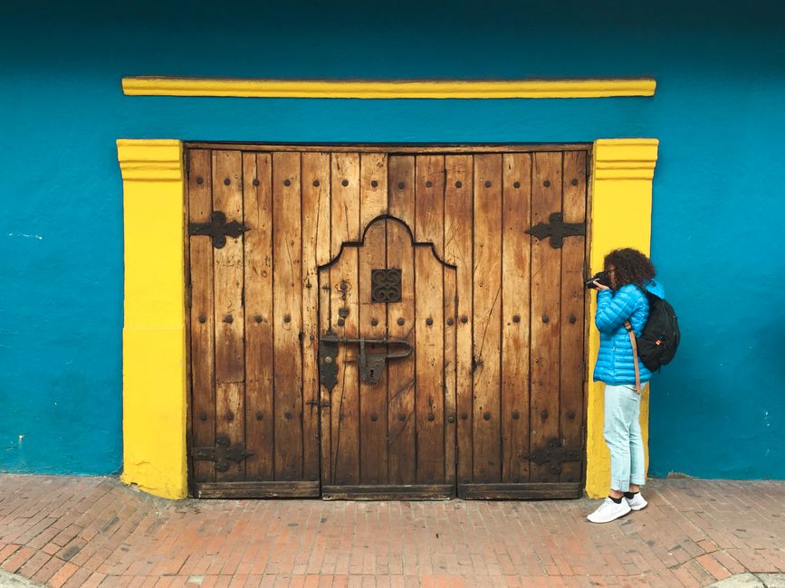 A woman explores a vibrant street in Bogotá featuring a rustic wooden doorway framed by bright colors.