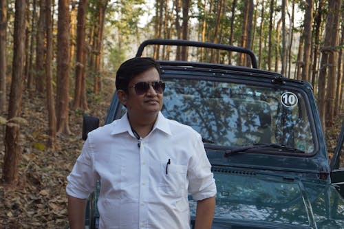 Man in White Long Sleeve Shirt Wearing Sunglasses Standing in Front of Vehicle