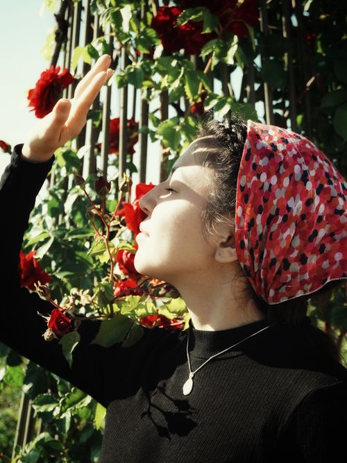 Free A woman with a red bandana embracing sunlight near vibrant rose blooms. Stock Photo