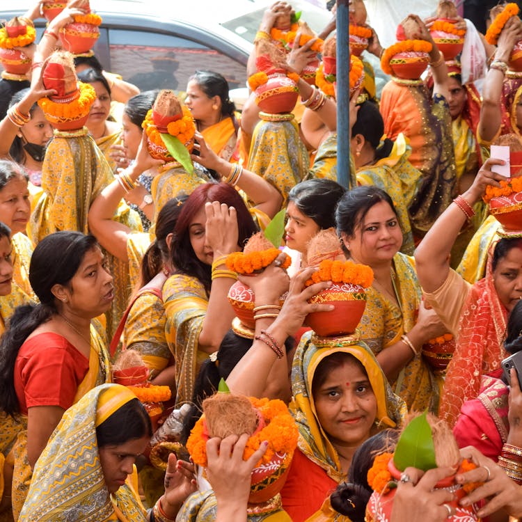 Crowd Of Women In Yellow Traditional Clothing Head Carrying Vases With Orange Wreaths During Festival Celebrations