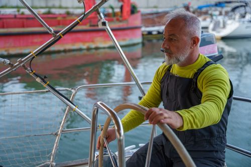 Free An experienced man steers a boat, focusing intently on the calm waterfront surroundings. Stock Photo