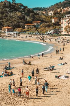 Beachgoers enjoy a sunny day with sea views and coastal town in the background.