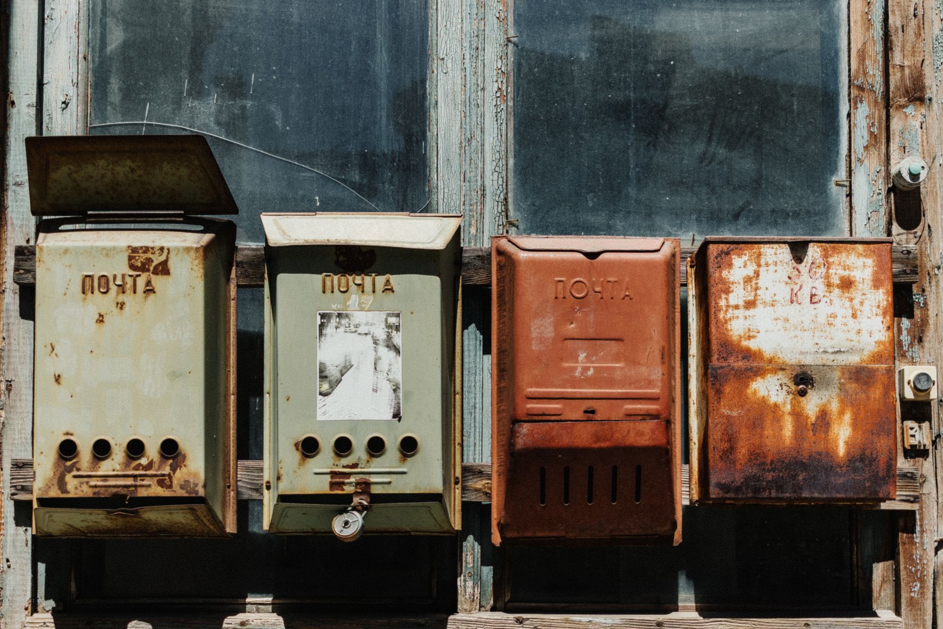A row of old, rusty mailboxes against a weathered wooden wall, showcasing a vintage aesthetic.