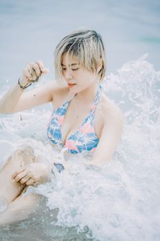 Asian woman enjoying a sunny day at the beach with splashes of refreshing water.