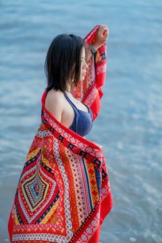 Woman standing by the ocean wrapped in a vibrant scarf, gazing into the distance.