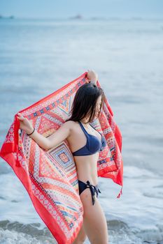 A woman in swimwear enjoying a day at the beach with a colorful shawl.