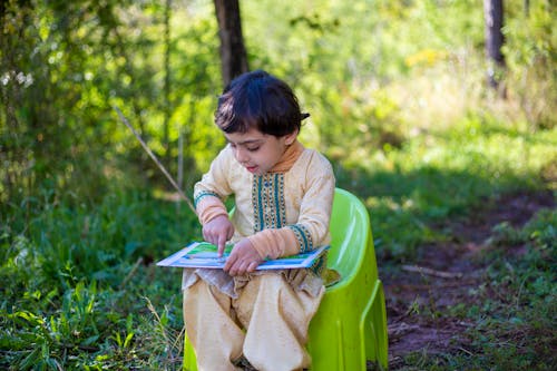 Free A Kid Sitting on the Plastic Chair While Reading a Book  Stock Photo