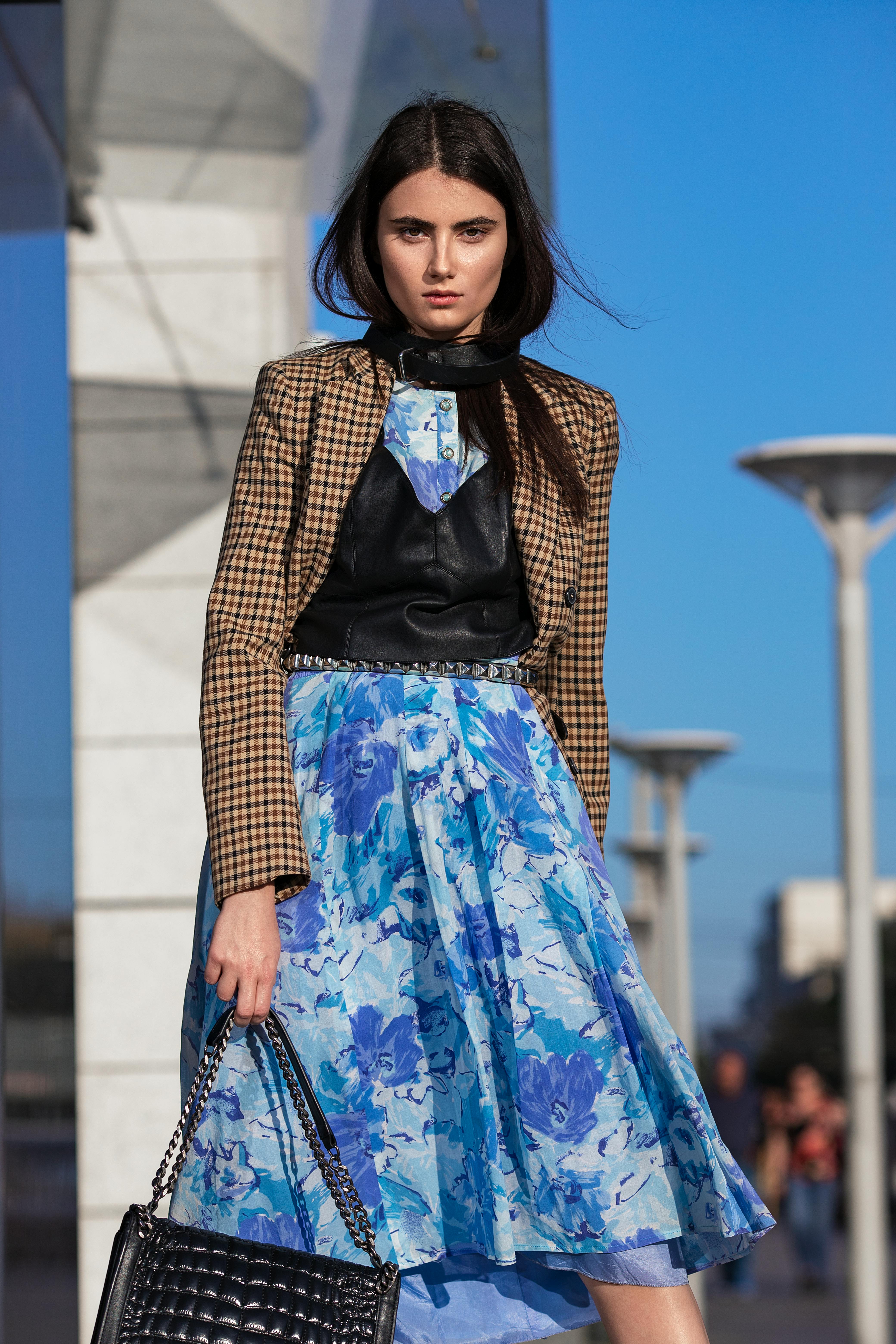 vertical fashion shot of woman in a floral blue skirt and beige checked suit against blue sky