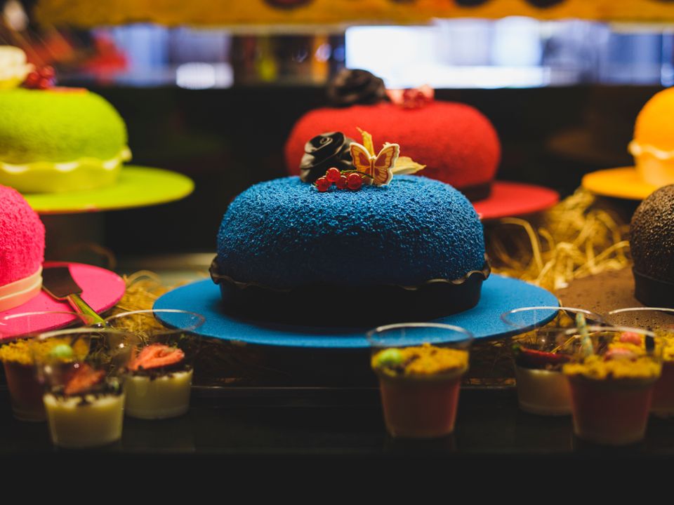 How to Price Your Baked Goods: The Complete Formula for Home Bakers in India (2026) 3 Assorted colourful decorated cakes and desserts on a table, showing the range of premium baked goods for sale.
