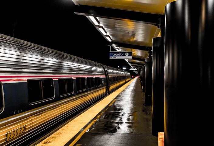 A sleek train parked at an illuminated station platform at night. Wet reflections on the ground.
