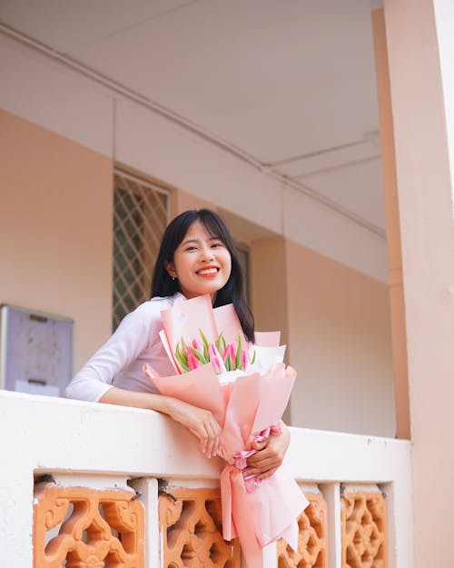 Woman in White Long Sleeve Shirt  Holding a Bouquet of Flowers 