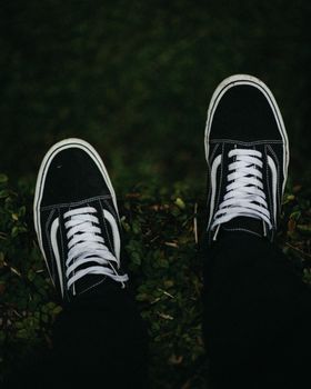 A close-up view of black sneakers with white laces on lush green grass outdoors.