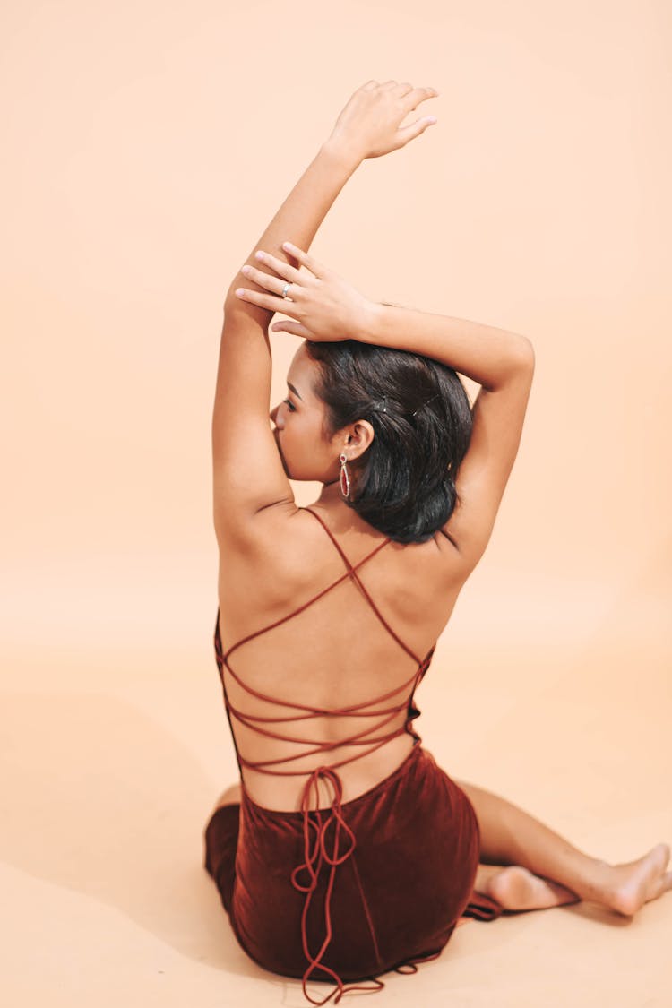 Back View Of A Woman In A Dress With Stripes Sitting On A Floor With Hands Raised