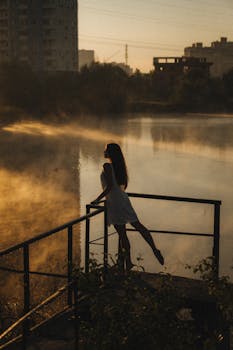 Beige Vertical Shot of a Woman in a Dress Leaning against Railing By a Pond in Urban Landscape