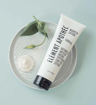 Element Apothec botanical lotion with CBD, surrounded by leaves and cream on a plate.