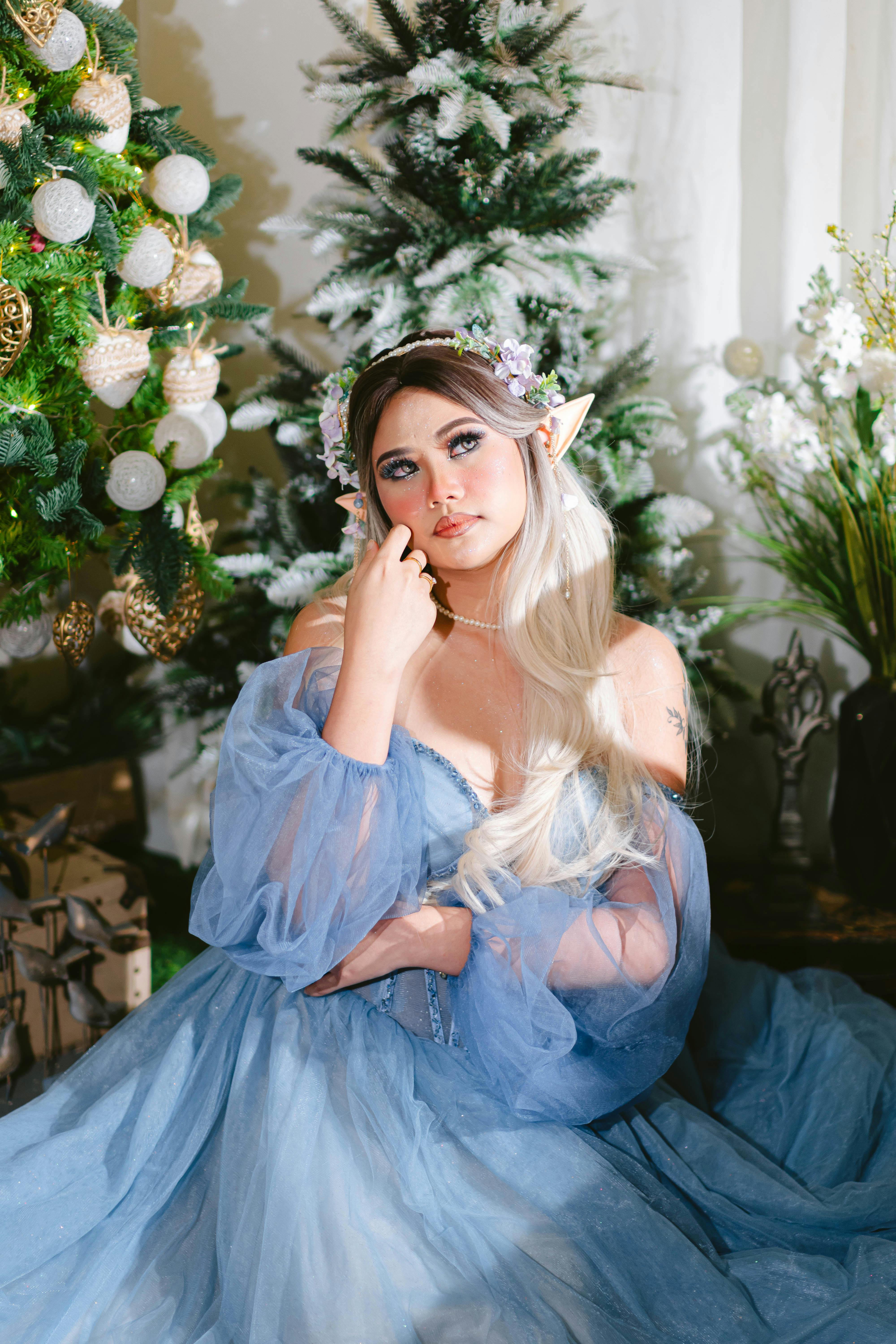 A woman in elf cosplay poses gracefully in a blue gown with Christmas decor.