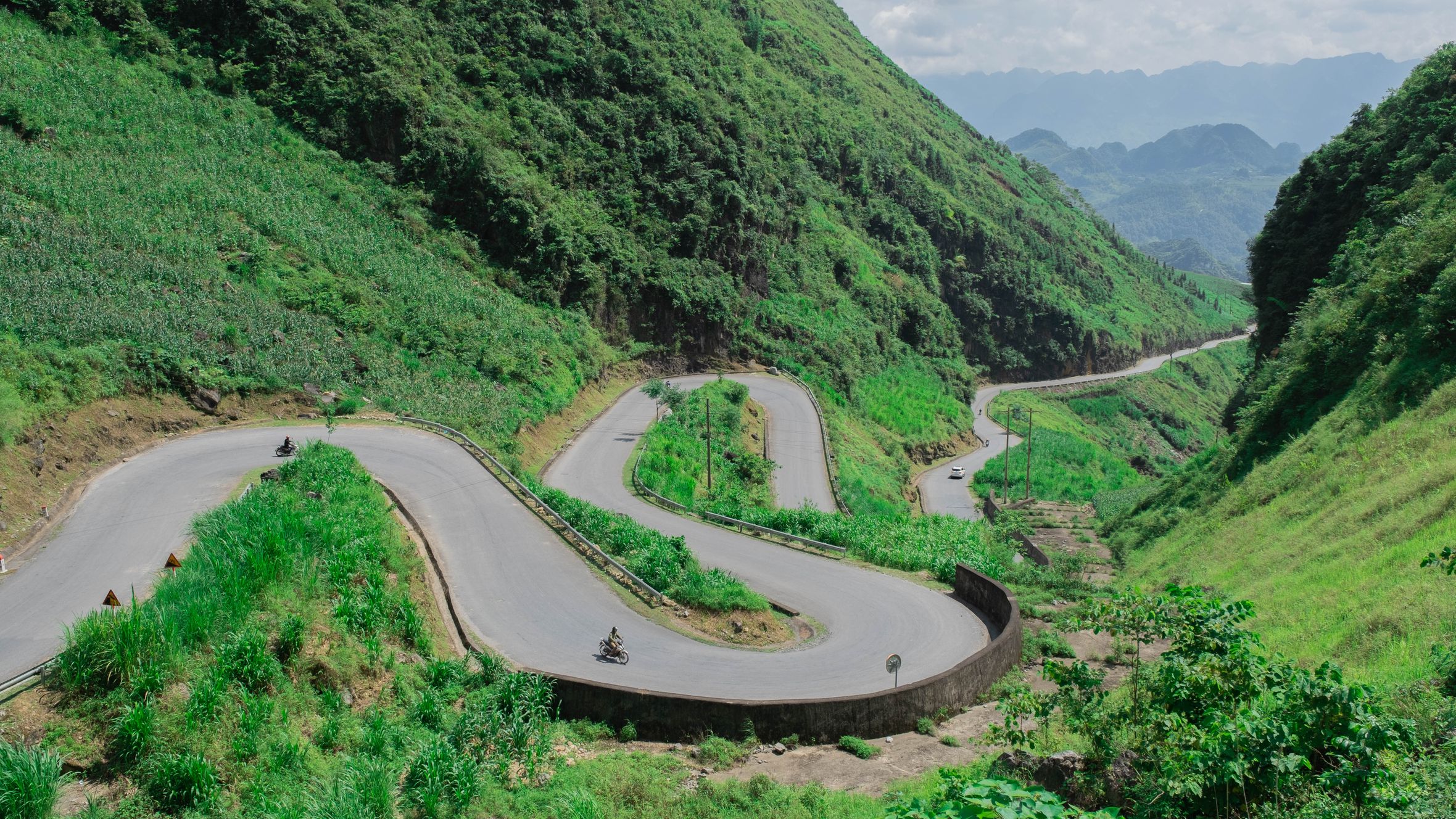Aerial view of a winding road cutting through lush green mountains in Hà Giang, Vietnam.