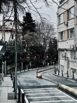 Empty urban street lined with residential buildings and leafless trees on a cloudy day.