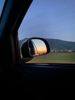 A beautiful sunset reflected in a car's side mirror with a mountainous backdrop.