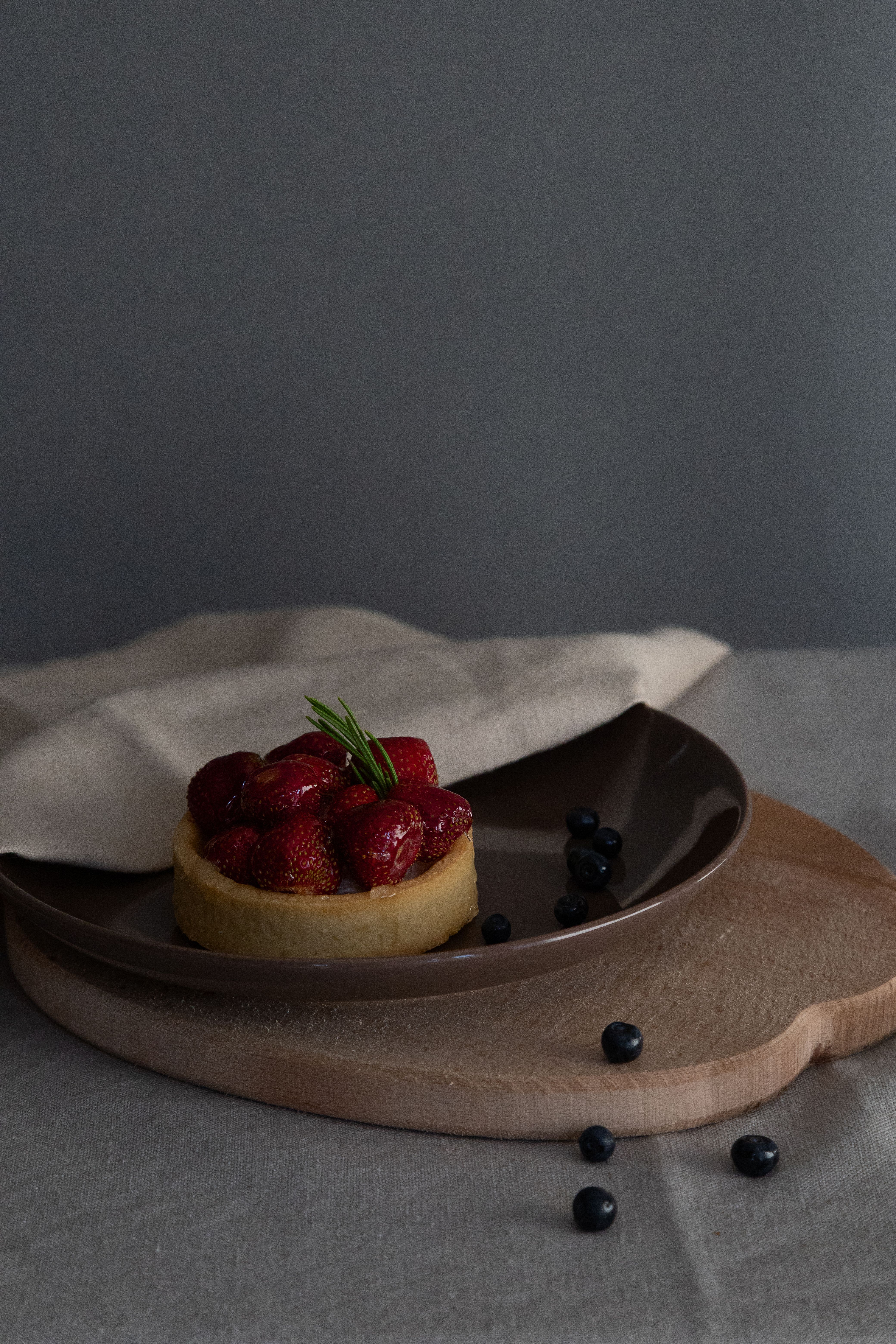 A delicious strawberry tart elegantly presented on a ceramic plate with blueberries.