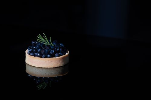 Free Close-up of a blueberry tart with rosemary garnish on a reflective black surface. Stock Photo