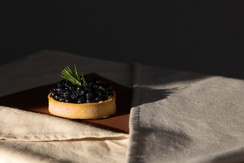 A Blueberry Tart on a Brown Surface Near the Cloth