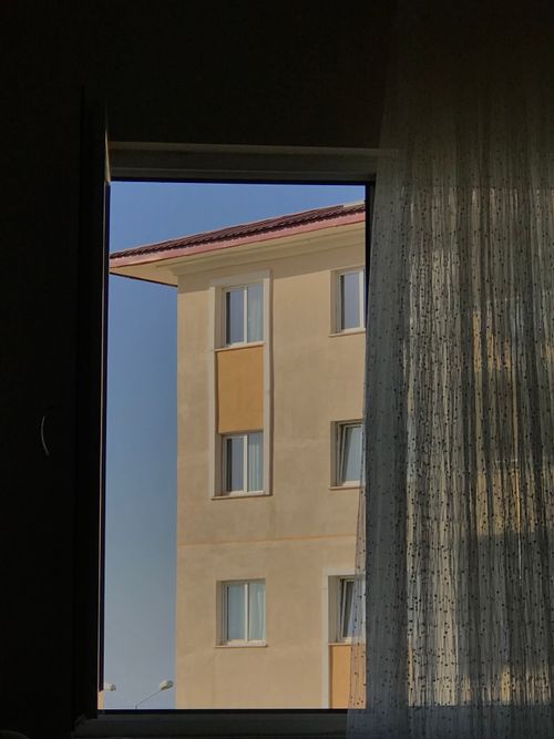 Free A modern building facade viewed through an open window with curtain drapes. Stock Photo