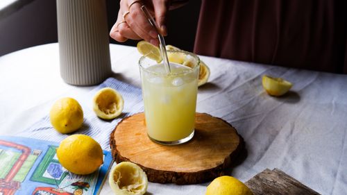 Free A glass of fresh lemon juice on a wooden board surrounded by whole and squeezed lemons. Stock Photo