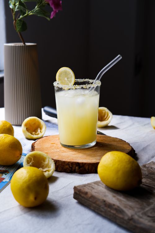 Free A glass of fresh lemonade with lemons and flowers arranged on a rustic table, offering a refreshing summer vibe. Stock Photo