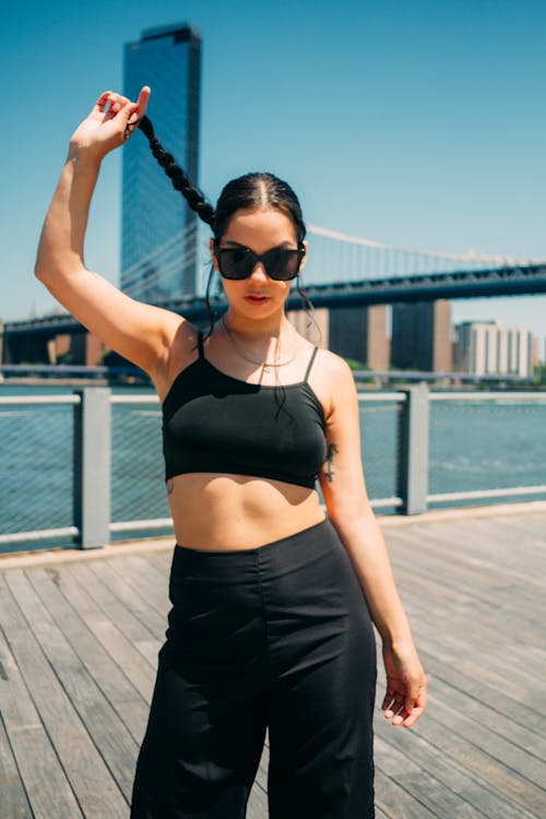 A Beautiful Woman in Black Crop Top and Pants Wearing Sunglasses while Holding Her Hair