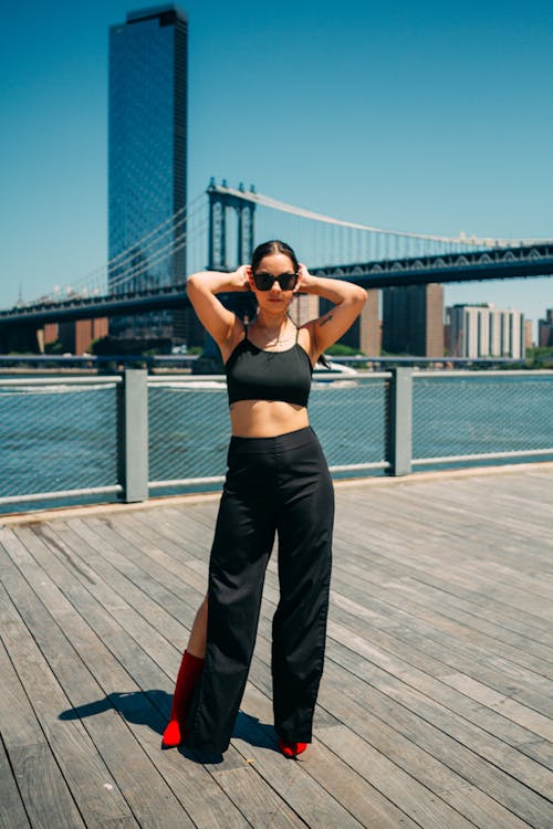 A Woman in Black Crop Top and Pants Standing on a Wooden Dock with Her Hands on Her Head