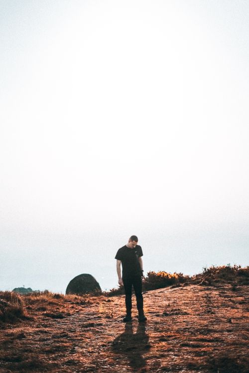Free A solitary man in black outfit stands in an open field under a clear sky, reflecting solitude. Stock Photo