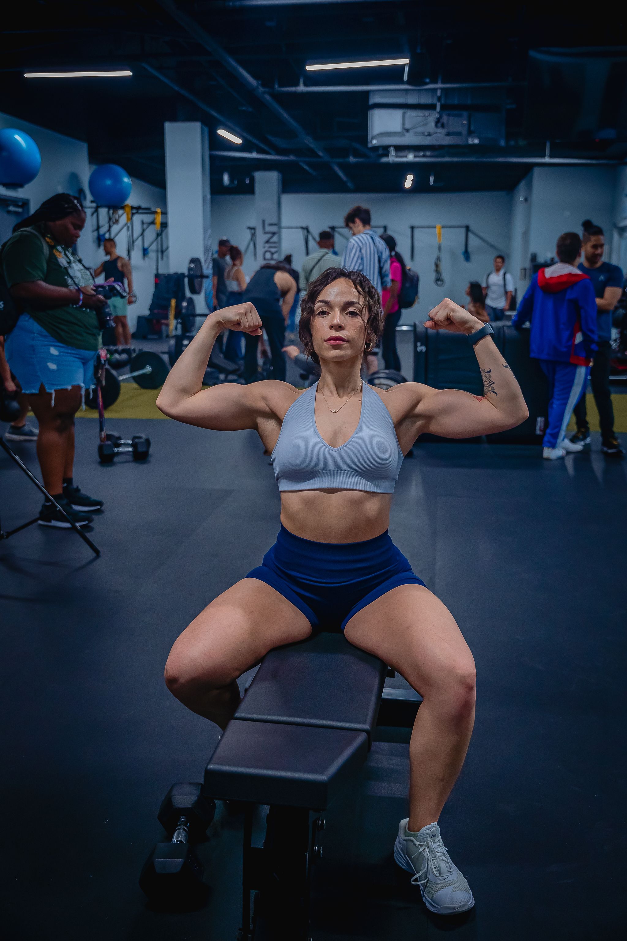 Adult woman in sports bra flexing muscles in a gym, showcasing strength and fitness focus.