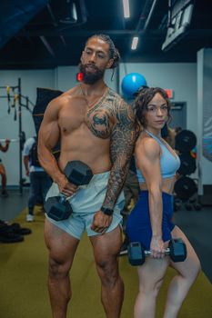 A muscular couple lifting dumbbells in a modern gym setting, showcasing fitness and strength.