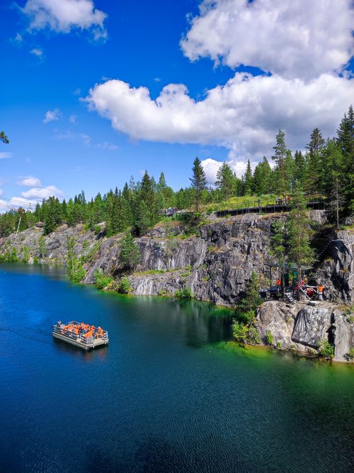 Free Picturesque view of a lake with rugged cliffs and a forest, featuring a boat under blue skies. Stock Photo